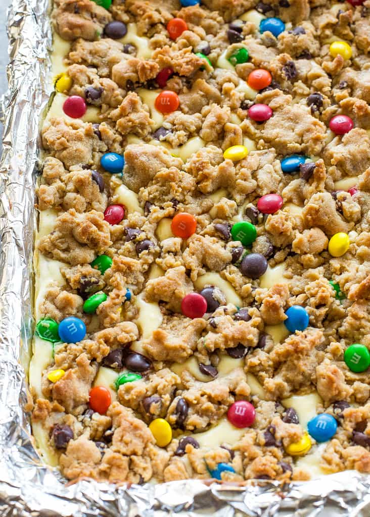 These Monster Cookie Cheesecake Bars have a layer of peanut butter, chocolate chips, oats, and M&M cookie bar with a layer of cheesecake in the middle. 
