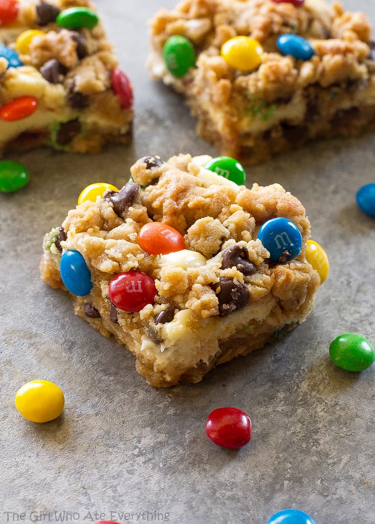 These Monster Cookie Cheesecake Bars have a layer of peanut butter, chocolate chips, oats, and M&M cookie bar with a layer of cheesecake in the middle. 