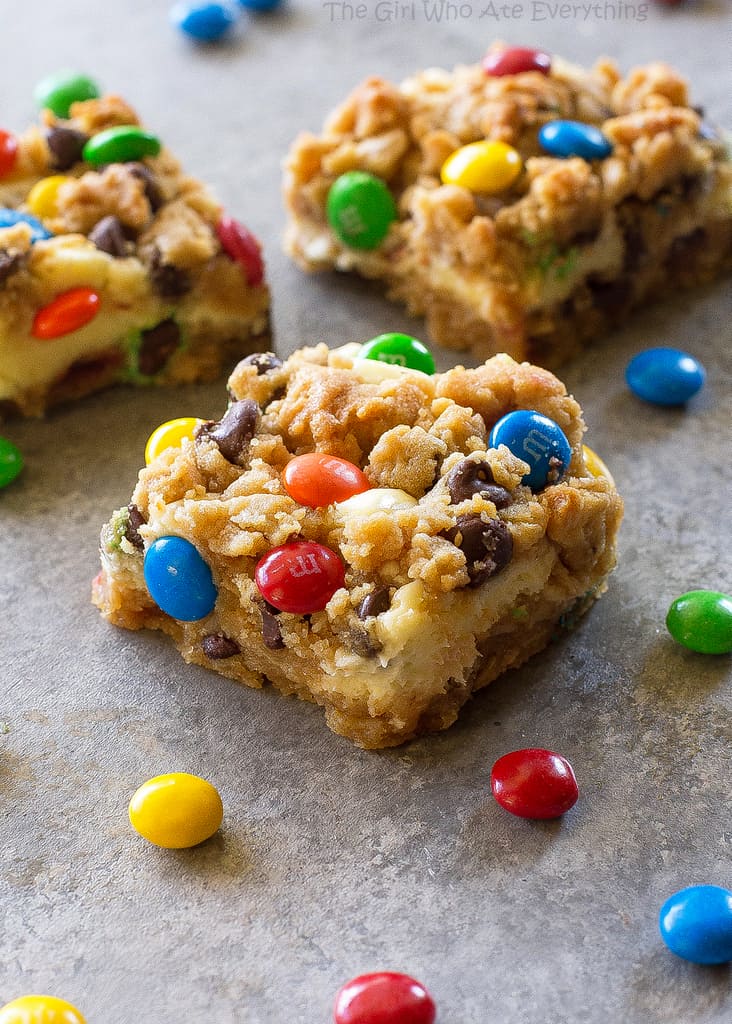 These Monster Cookie Cheesecake Bars have a layer of peanut butter, chocolate chips, oats, and M&M cookie bar with a layer of cheesecake in the middle.